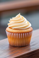 A single vanilla cupcake with creamy frosting sits on a wooden surface