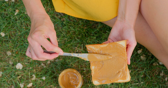 Woman spreading peanut butter on toast while sitting on grass in park
