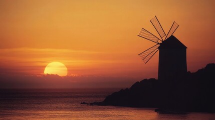 Silhouette of a wind mill at sunset over a tranquil sea.