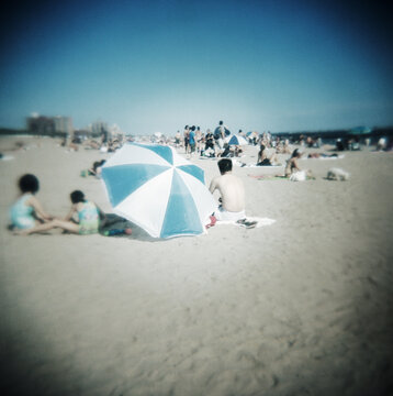 Tourists on the beach with beach umbrella, Coney Island, Brooklyn, United States 