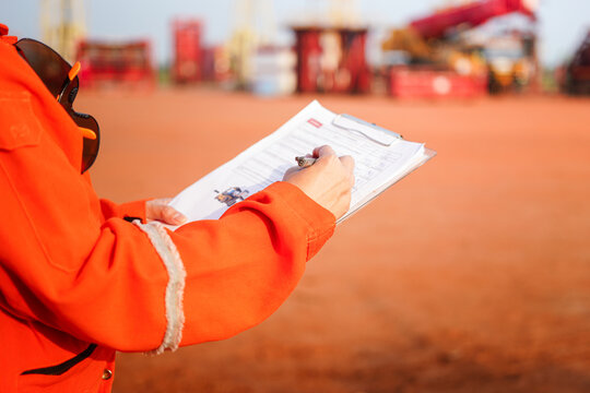 A maintenance engineer is checking on checklist to verify the condition of forklift or heavy machine vehicle, with background of construction site workplace. Industrial working scene, close-up.