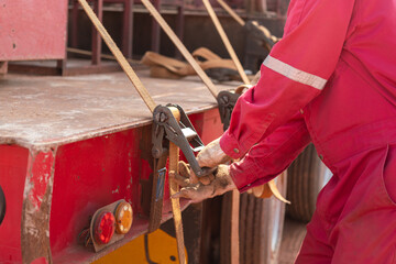 Action of a worker is tightening latching strap belt to secure the load object on trailer truck....
