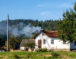 Fototapeta premium Rustic white house with smoke from chimney, idyllic rural landscape.