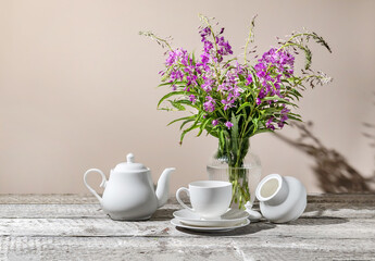 Still life with a white cup of tea, a teapot, sugar, a bouquet of purple wildflowers on a wooden table
