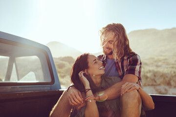 Young mixed couple on a date in a truck bed of an old timer truck on a road trip on a sandy beach near the ocean