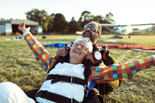 Happy senior woman celebrating after tandem skydive landing on grass field