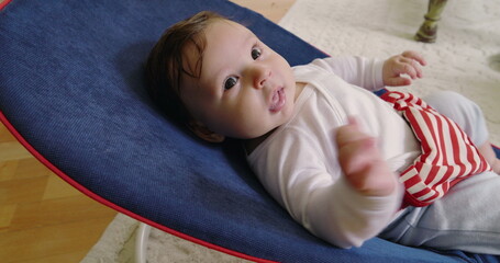 Baby lying in a bouncer, calmly gazing upwards, enjoying a moment of relaxation and comfort in a cozy home environment, showcasing the innocence and serenity of early childhood