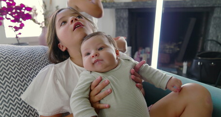 Girl handing baby sibling to parent on the couch, the playful and loving interaction showcases the...