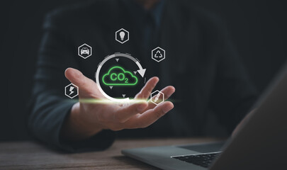 Businessman holding virtual CO2 icon surrounded by eco-friendly symbols, representing carbon footprint reduction, sustainable energy, and environmental responsibility in modern business practices.