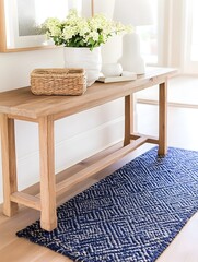 A long, light wood console table holds flowers, a basket, and books. A navy blue and beige geometric rug sits beneath