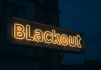A vibrant neon sign displaying the word "Blackout" against a dark, evening sky backdrop.