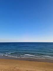 Fototapeta premium Horizon view of a beautiful deserted golden sand beach, ocean waves and blue sky, landscape of Portugal