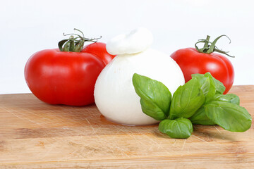 A closed ball of burrata cheese on a wooden cutting board with fresh basil leaves, rustic and fresh presentation