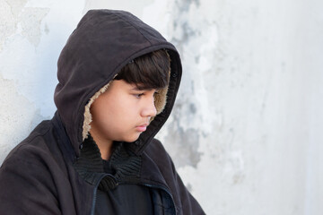 Asian teenboy in black hoodie is sitting on dirty floor and messy wall of an abandoned building,...