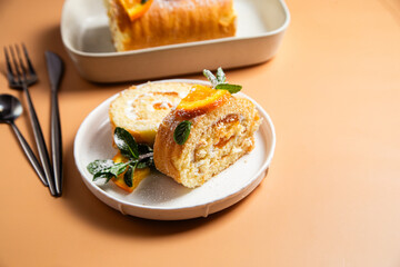 Orange sponge roll with cream and mint in a white plate on a bright background