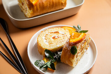 Orange sponge roll with cream and mint in a white plate on a bright background