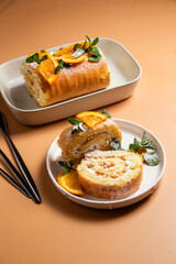 Orange sponge roll with cream and mint in a white plate on a bright background