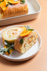 Orange sponge roll with cream and mint in a white plate on a bright background