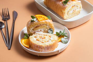 Orange sponge roll with cream and mint in a white plate on a bright background