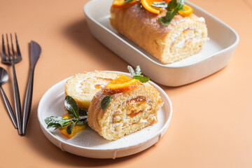 Orange sponge roll with cream and mint in a white plate on a bright background