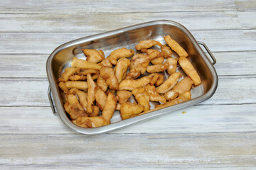 A tray of fried chicken is sitting on a wooden table. The chicken is golden brown and he is cooked