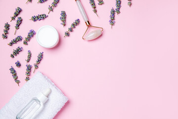 A flat lay of essential skincare items, including a jade roller, moisturizer, and dropper bottle, surrounded by lavender on a soft pink background. Perfect for beauty and wellness themes.
