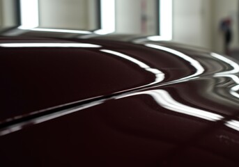 Deep Maroon Car Hood Gleaming Under Bright Studio Lights, Smooth Curves and Reflections Showcase Perfect Paint Job