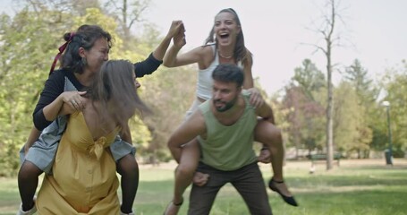 Friends having fun and enjoying a sunny day in the park. They give each other piggyback rides and laugh.