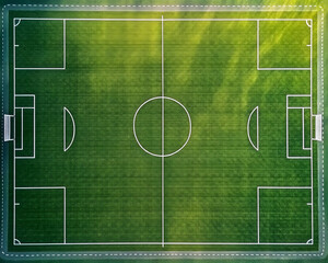 Aerial view of a green football field with white lines, empty except for a few players training in the distance, captured from directly overhead by a drone