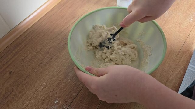 close-up hands in process of making dough for frying pancakes or cakes, pie. girl mixing batter baking, stirs it with black spoon in plastic bowl. child baking video pancake preparation
