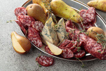 Blue cheese, dry-cured sausages, thyme and pears on a stone table.