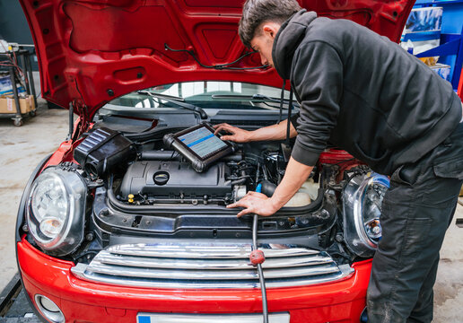 Mechanic diagnosing car engine problems using diagnostic software on tablet