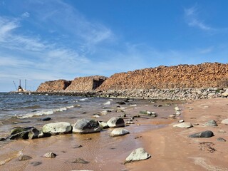 Massive timber stockpile on Baltic Sea shoreline near port facility, symbol of forestry export and industrial presence in natural coastal environment