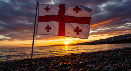 Georgian flag waving on pebble beach at dramatic sunset over the Batumi Black sea. National flag against beautiful coastal landscape. Independence day of Georgia