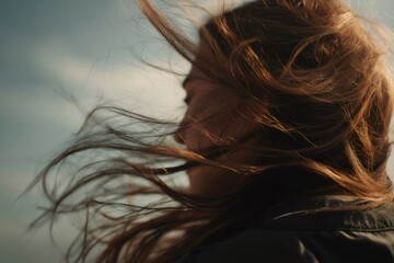 Long brown hair of a young woman blowing in the wind in slow motion, creating a sense of freedom and movement against a cloudy sky