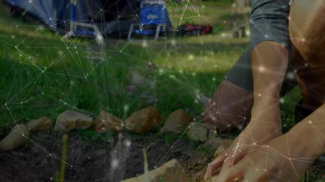 Marketing professional kneeling at forest campsite, analyzing network overlay connecting gear icons