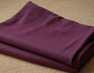 A folded burgundy fabric rests on a textured surface, showcasing its soft and smooth finish.