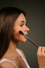 Obraz premium Woman applies makeup with a brush while posing elegantly in a soft light setting