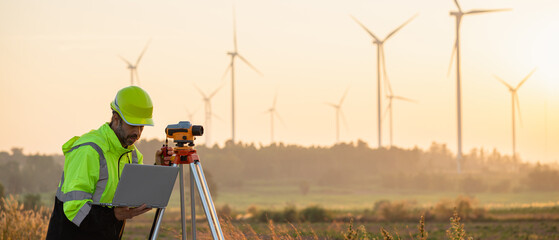 A field engineer surveys the land at sunset, with wind turbines behind as technology meets clean...