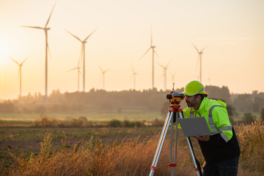 A field engineer surveys the land at sunset, with wind turbines behind as technology meets clean energy.