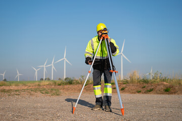 Surveying the land with high-precision tools, a field engineer works against a backdrop of wind turbines-where technology meets clean energy innovation.