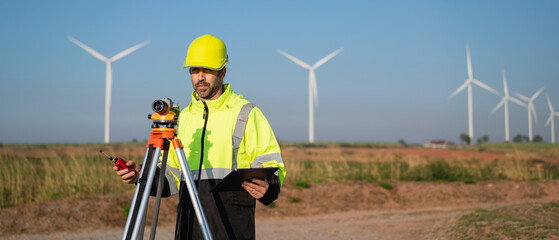 Surveying the land with high-precision tools, a field engineer works against a backdrop of wind...