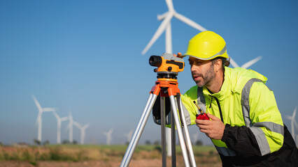 Surveying the land with high-precision tools, a field engineer works against a backdrop of wind turbines-where technology meets clean energy innovation.