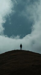 Solitary figure on a hilltop under a cloudy sky.