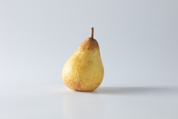 A ripe yellow pear stands alone against a clean white background, captured in soft natural light. This minimalist studio shot highlights its texture and form with elegant simplicity © Pedro