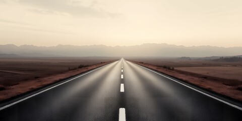 A long straight asphalt road stretching into the horizon with mountains in the background