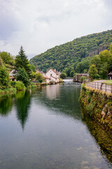 Traditional riverside houses reflecting in the calm water in the picturesque town of Ornans, France, along the Via Francigena.