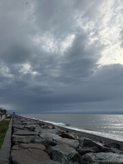 Fototapeta premium Rocky shore with storm clouds and waves on a cloudy day. View includes sea, rocks, beach, and overcast sky.