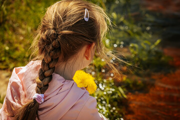 Naklejka premium A young girl in a pink jacket sits quietly by the edge of a sunlit river, surrounded by fresh spring greenery and shimmering water.