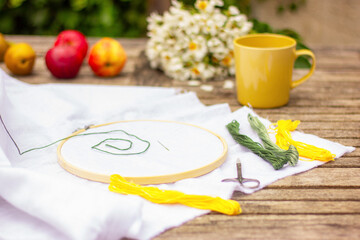 embroidery kit and white fabric, yellow cup, fruits and flowers on the wooden table